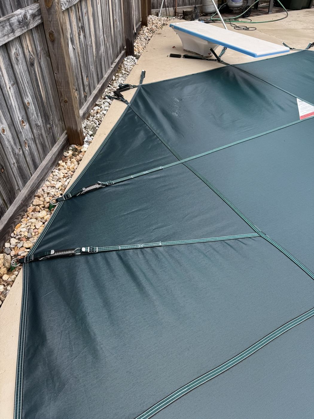 A green safety cover pulled tight against a wooden fence next to a diving board.