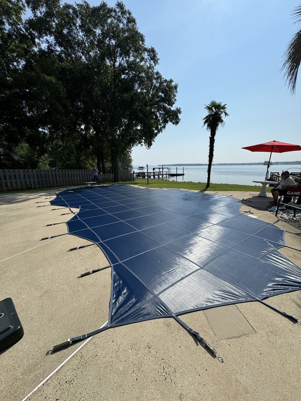 A blue safety cover on a freeform pool looking out over a lake.