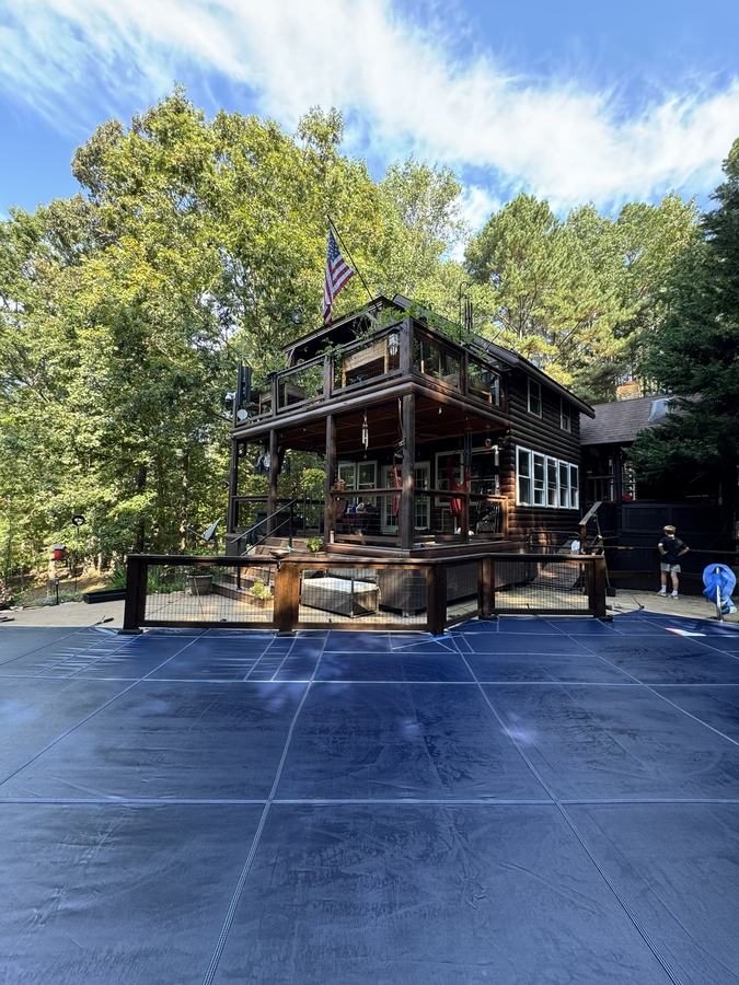 A blue safety cover on a pool below a large wooden home.
