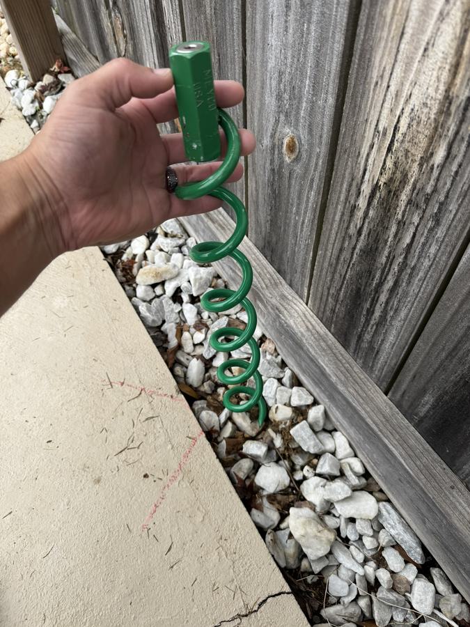 A hand holding a cover spring with a green sleeve beside a wooden fence.