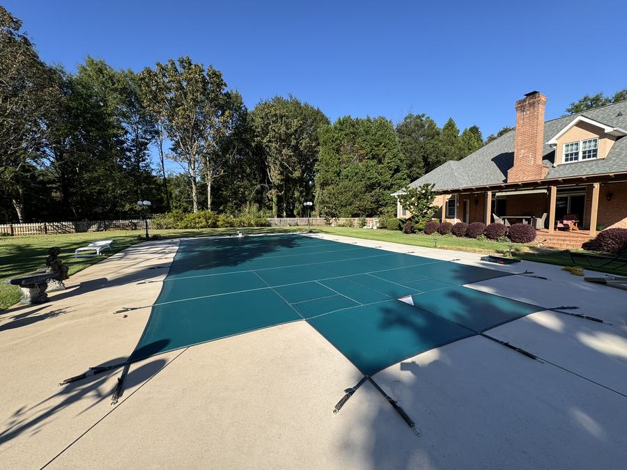 A teal safety cover on a pool beside a brick home with a chimney.