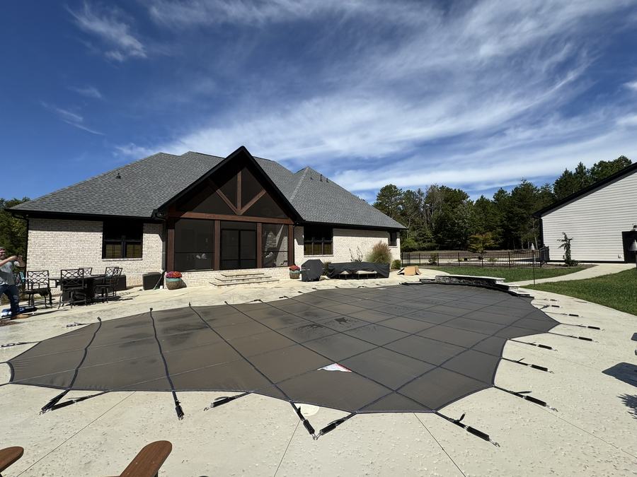 A dark gray safety cover on a large freeform pool behind a stone and timber home.