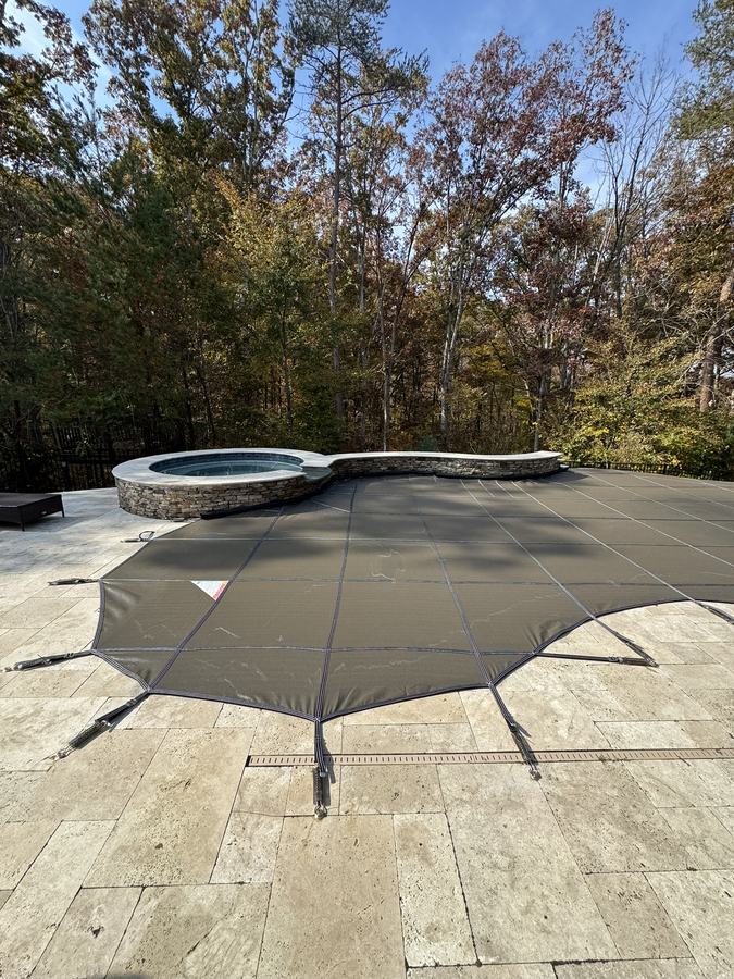 A gray safety cover shaped around a raised round spa on a stone deck.