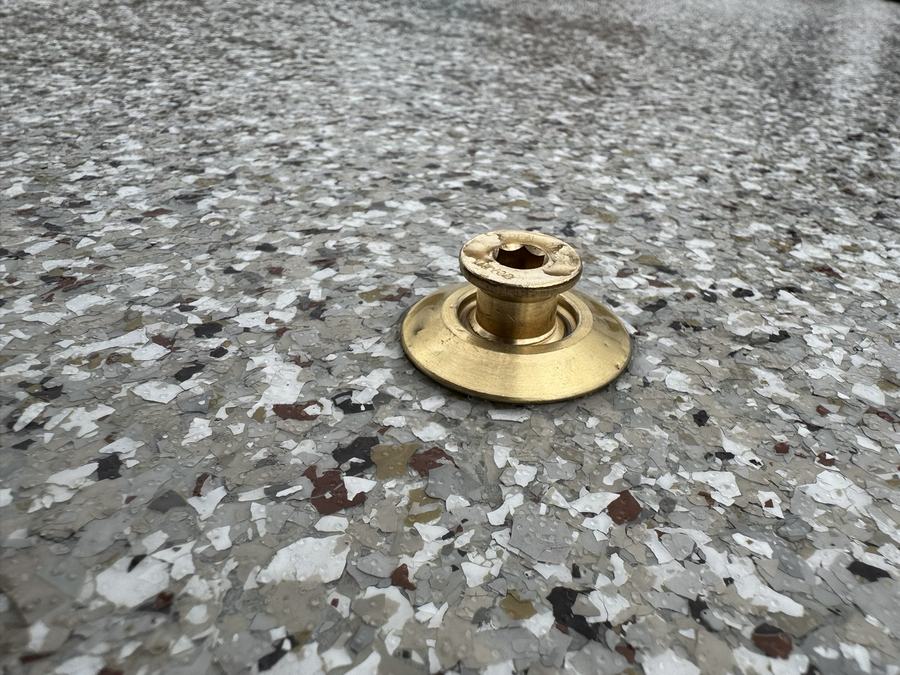 A brass cover anchor set flush into a concrete patio with an epoxy finish.
