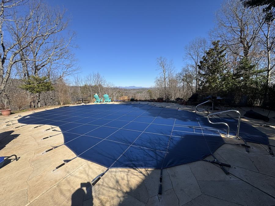 A blue safety cover on a freeform pool looking out over a lake and the mountains.