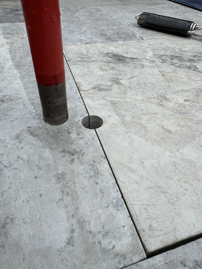 A core drill bit sitting in a freshly drilled anchor hole in a travertine deck.