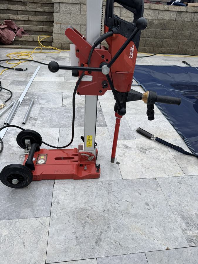 A core drill set up on a travertine pool deck to drill anchor holes.