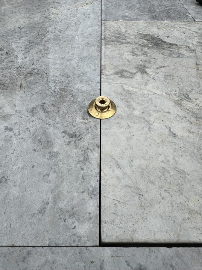 A brass cover anchor sitting flush in a travertine pool deck.