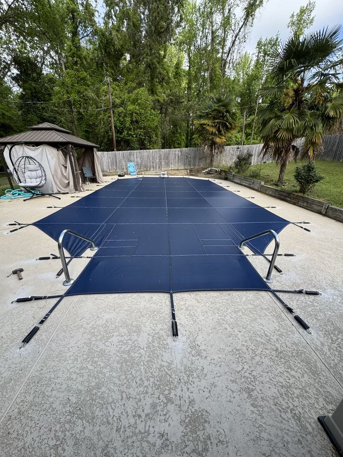 A navy safety cover on a rectangular pool beside a gazebo.