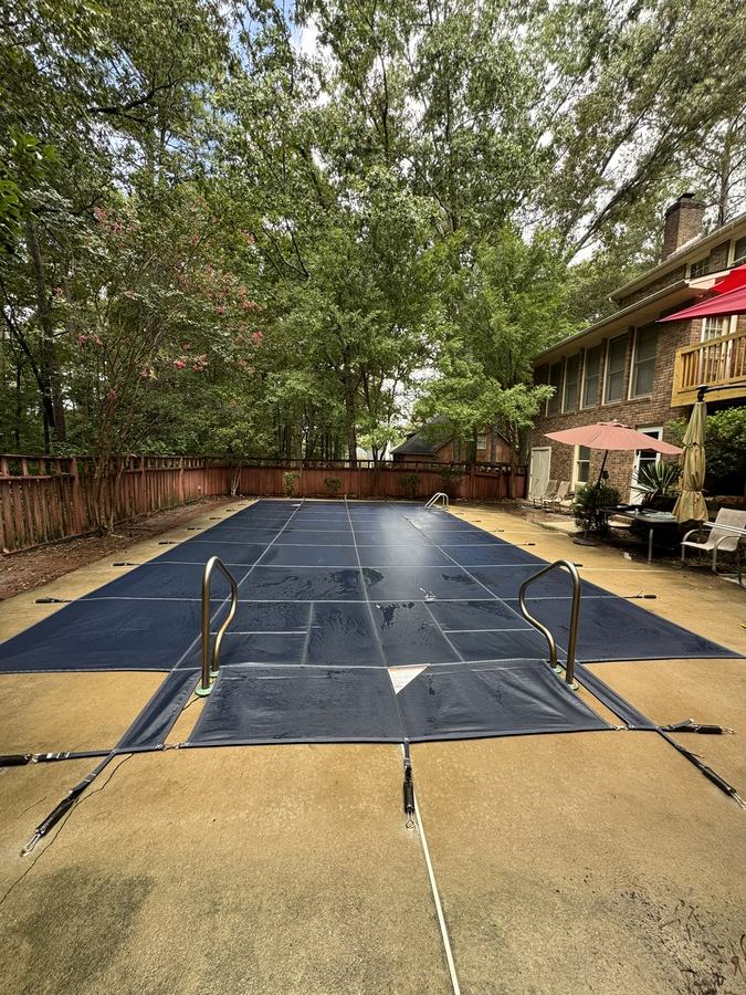 A navy safety cover on a rectangular pool with a tan concrete deck.