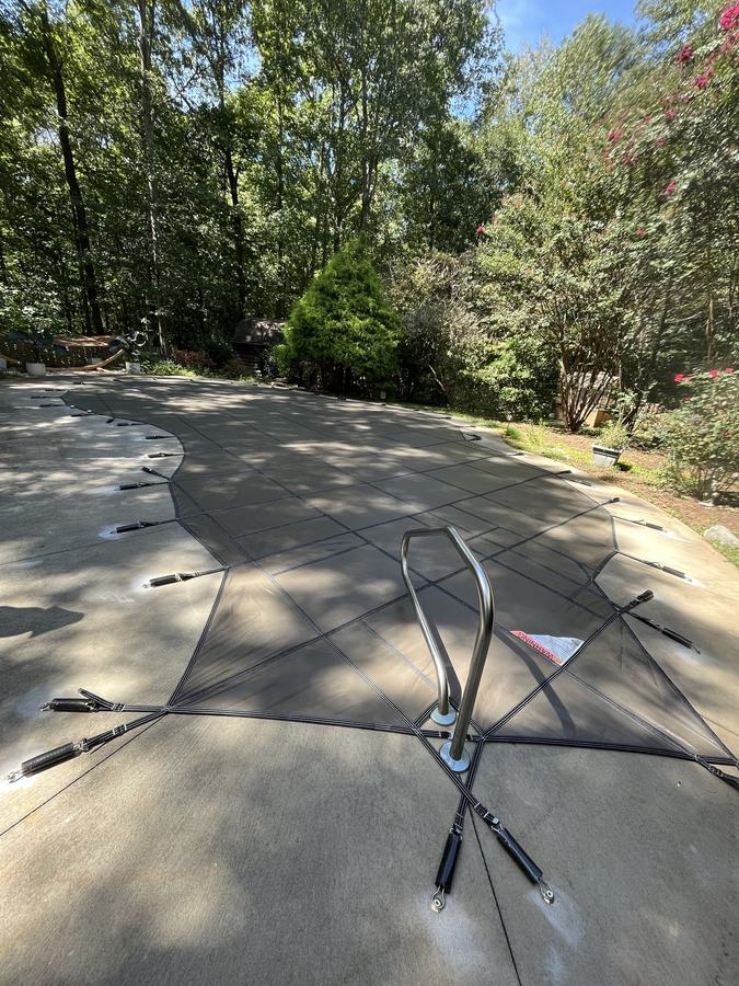 A gray safety cover fitted around a pool handrail on a shaded deck.