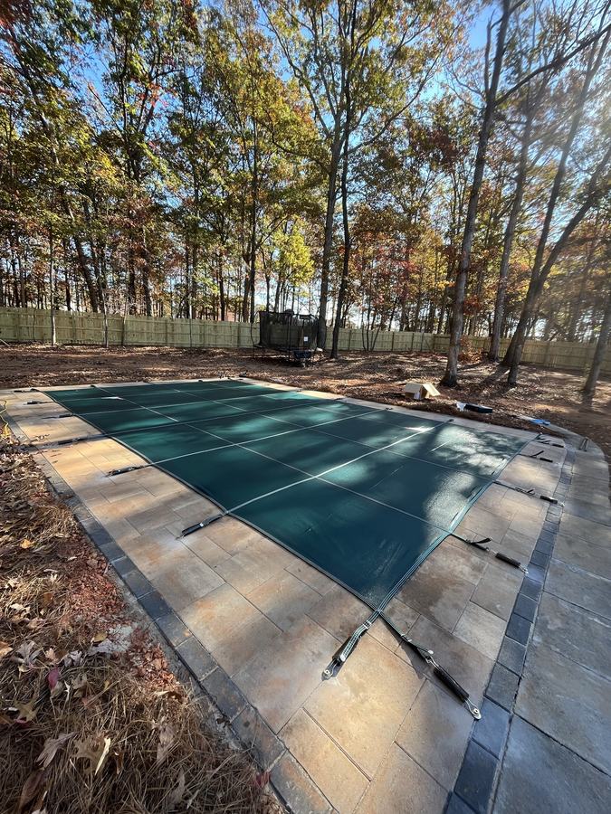 A green safety cover on a rectangular pool in an autumn yard.