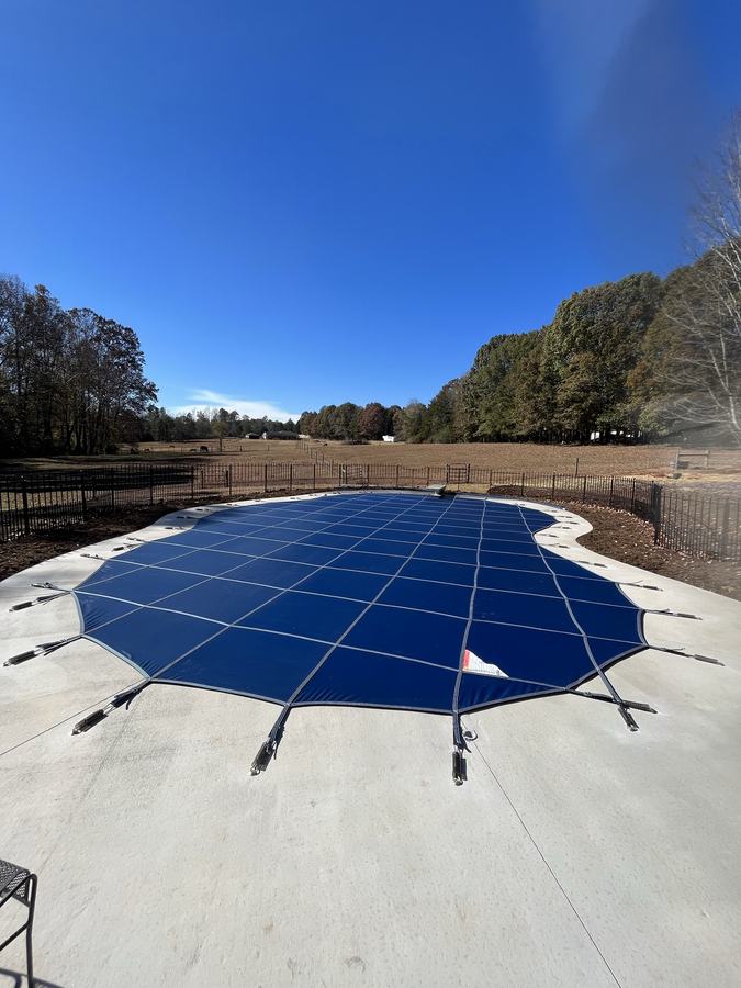 A blue safety cover on a freeform pool with a concrete deck.
