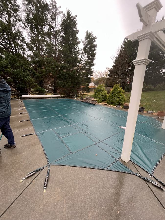 A green safety cover on a pool beside a white porch column.