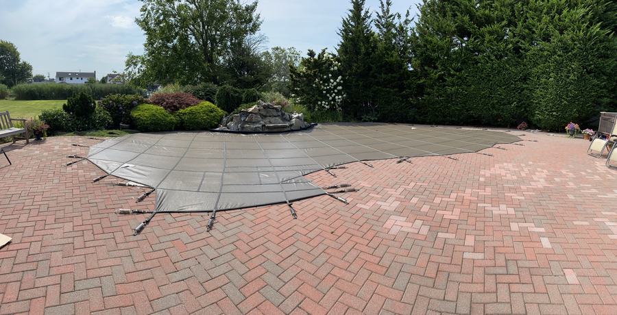 A gray safety cover on a freeform pool with a herringbone brick deck.