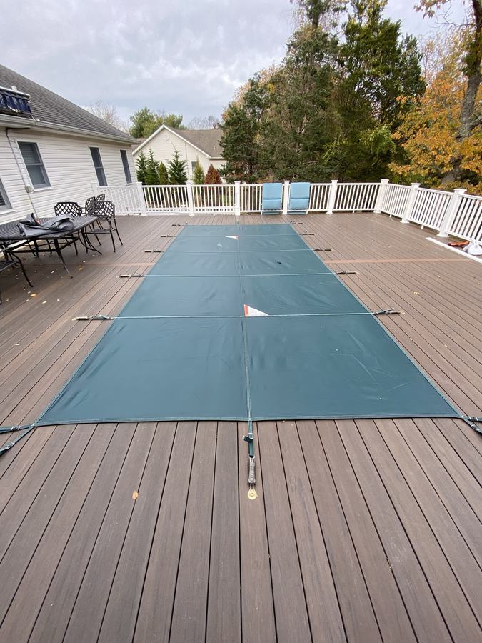 A green safety cover on a rectangular pool surrounded by composite decking.