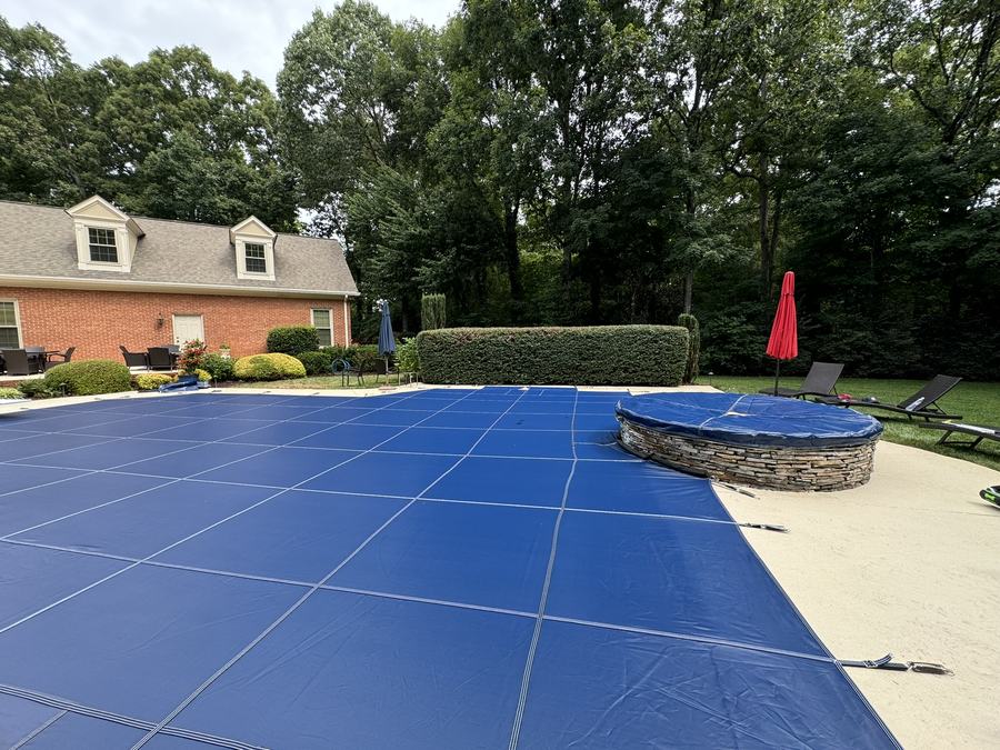 A blue safety cover on a rectangular pool with a raised round spa.