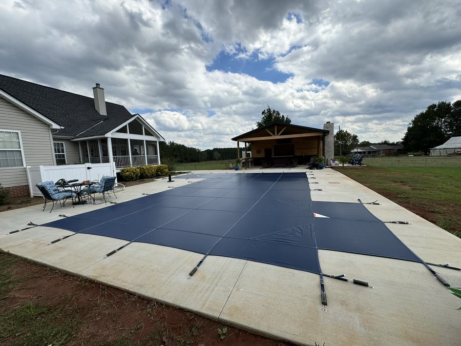 A navy safety cover on a rectangular pool behind a home with a covered patio.