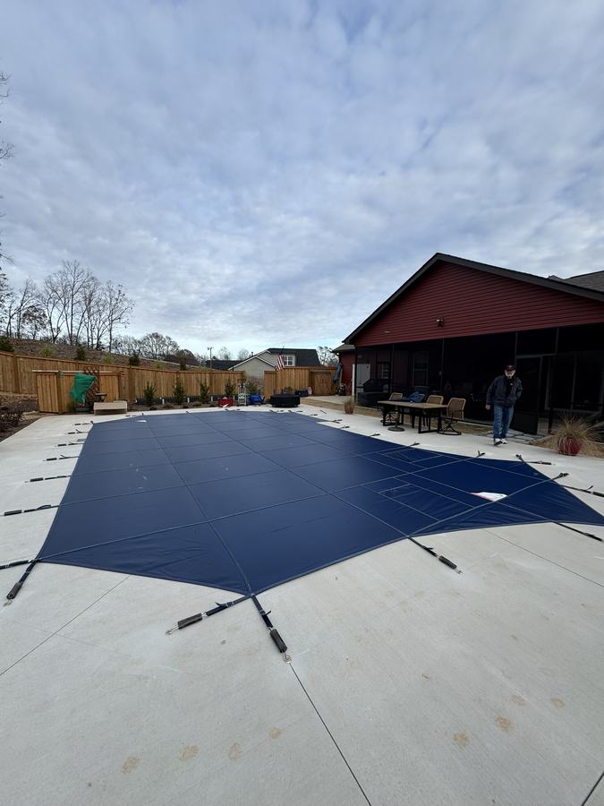A navy safety cover on a rectangular pool beside a red barn-style building.